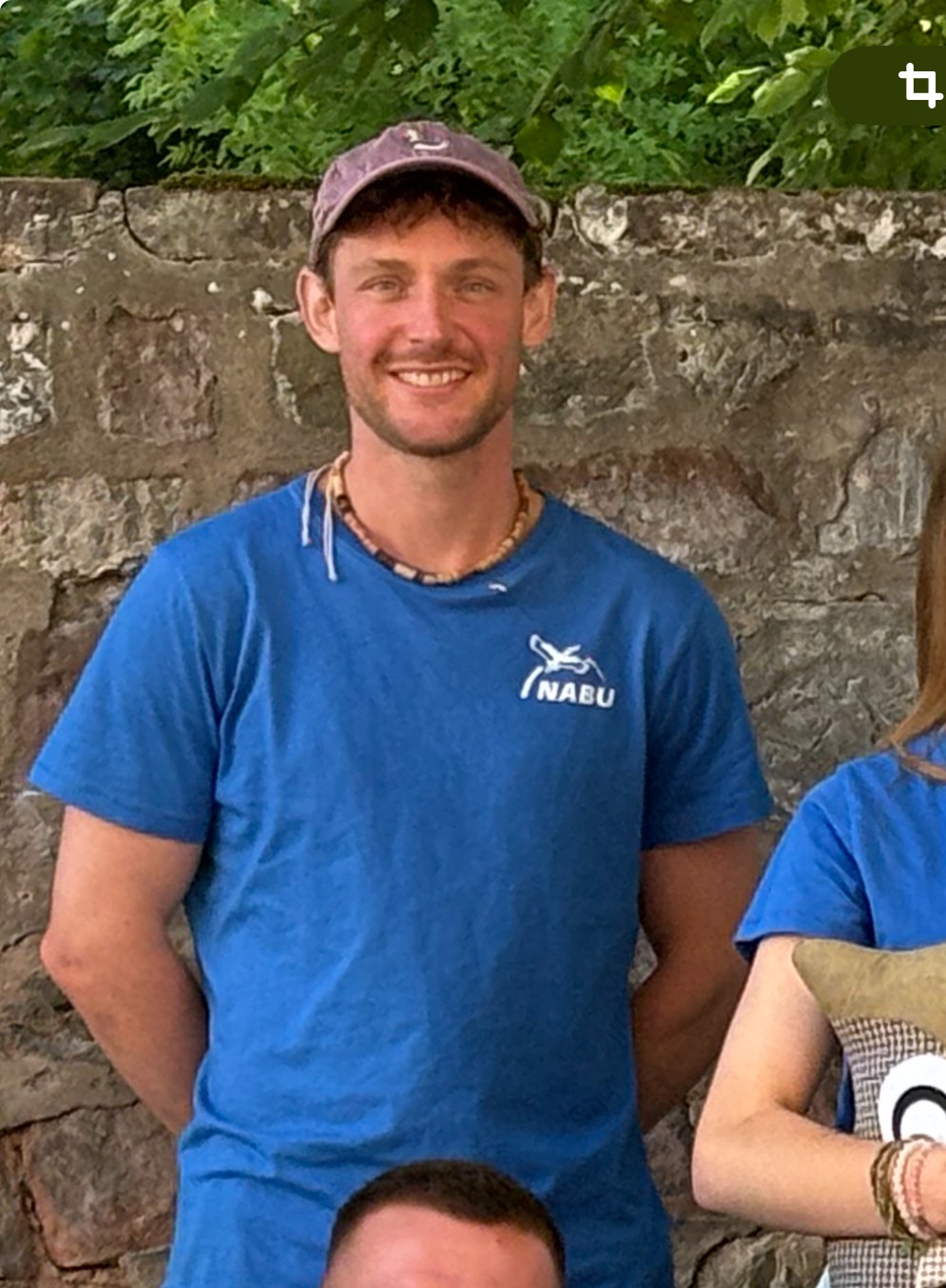 Jens Wollenweber ist Naturschützer mit Überzeugung. Als aktives NABU-Mitglied lebt er Nachhaltigkeit nicht nur im Alltag, sondern auch auf dem Feld – mit seiner Zukunfts-Patenschaft für das Lila Dreieck auf der Acht unterstützt er aktiv die Renaturierung von Brachflächen in der Moselregion. Jens Wollenweber, NABU-Mitglied, steht vor einer Natursteinmauer. Er trägt ein blaues NABU-Shirt, eine lila Kappe und lächelt in die Kamera.